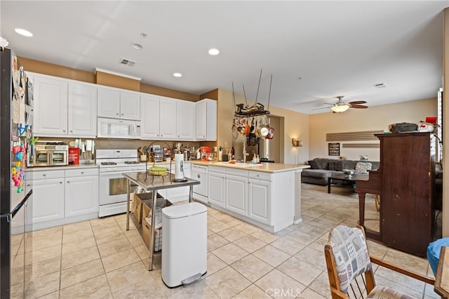 kitchen with a peninsula, white appliances, open floor plan, ceiling fan, and white cabinets