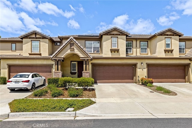 multi unit property with roof mounted solar panels, an attached garage, and concrete driveway