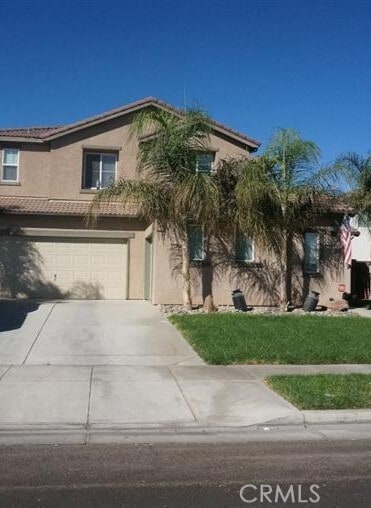 view of front of house with a tiled roof, driveway, a front lawn, an attached garage, and stucco siding