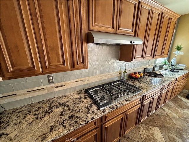 kitchen with stainless steel gas cooktop, stone countertops, under cabinet range hood, and brown cabinetry