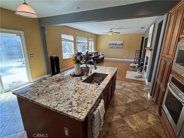 kitchen featuring light stone countertops, a sink, baseboards, a fireplace with raised hearth, and stainless steel appliances