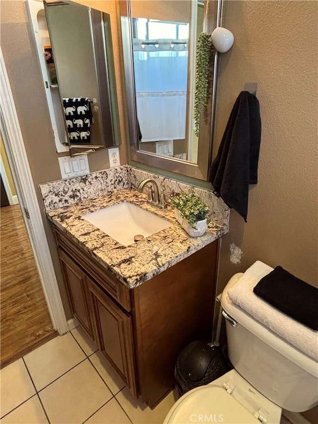 half bathroom featuring tile patterned floors, a textured wall, vanity, and toilet