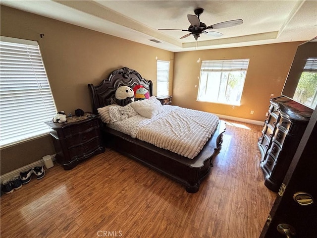 bedroom featuring ceiling fan, visible vents, wood finished floors, a raised ceiling, and baseboards
