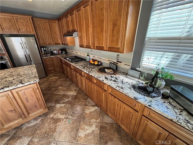 kitchen featuring freestanding refrigerator, wall oven, gas stovetop, under cabinet range hood, and brown cabinets