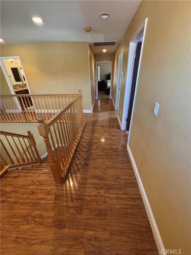 hallway featuring baseboards, recessed lighting, wood finished floors, and an upstairs landing