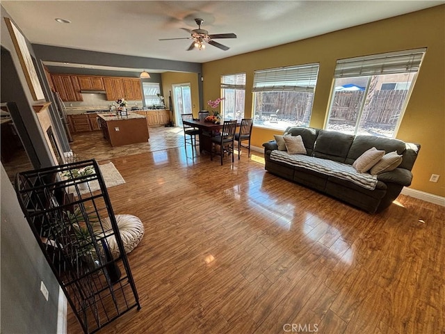 living area featuring a ceiling fan, baseboards, and wood finished floors