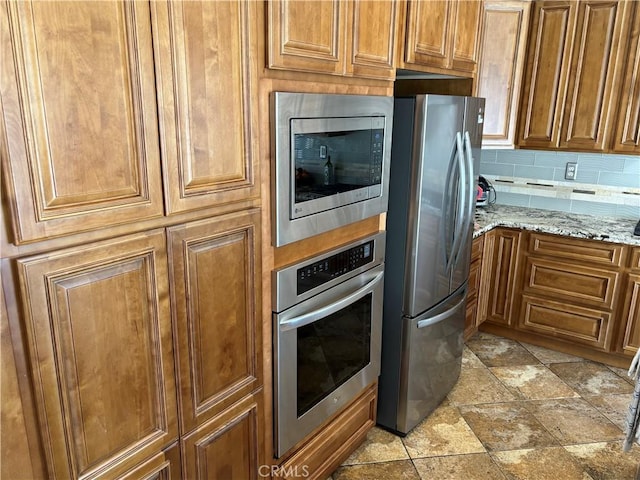 kitchen featuring light stone counters, stone finish flooring, brown cabinets, and stainless steel appliances