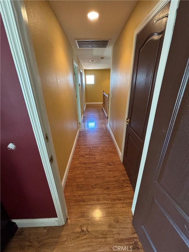 hallway with baseboards, visible vents, and wood finished floors