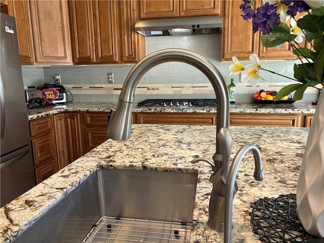 kitchen with freestanding refrigerator, decorative backsplash, under cabinet range hood, and light stone countertops