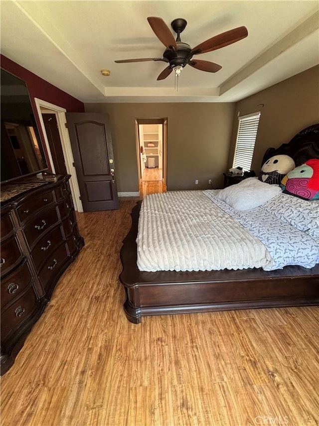 bedroom with baseboards, ceiling fan, wood finished floors, and a tray ceiling