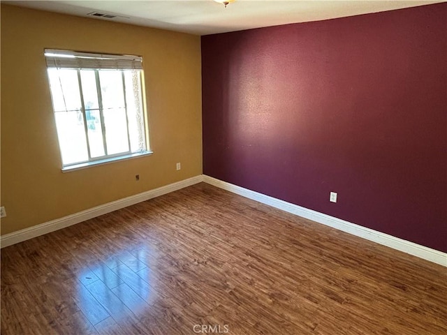 unfurnished room featuring baseboards, wood finished floors, and visible vents