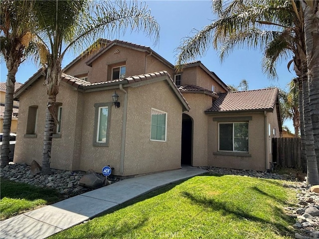 mediterranean / spanish-style home featuring a front lawn, stucco siding, a tiled roof, and fence