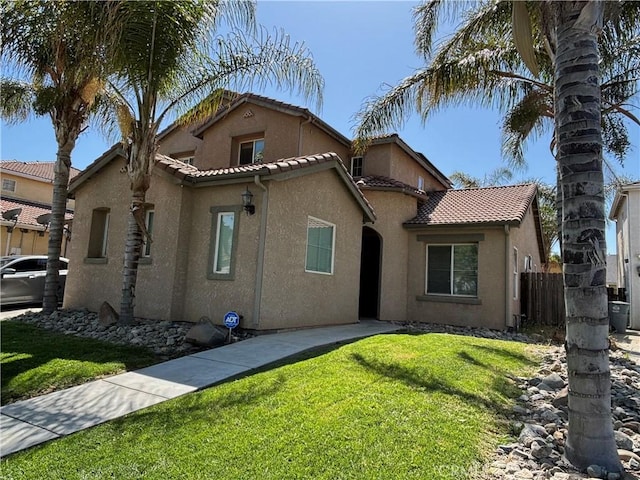 mediterranean / spanish home with a front lawn, stucco siding, a tile roof, and fence