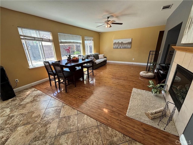 dining room with a tiled fireplace, baseboards, a ceiling fan, and visible vents