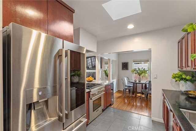 kitchen with a skylight, appliances with stainless steel finishes, dark stone countertops, recessed lighting, and light tile patterned flooring