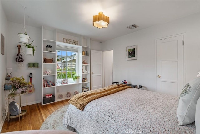 bedroom with baseboards, wood finished floors, and visible vents