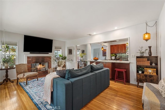 living room featuring recessed lighting, baseboards, a brick fireplace, and light wood finished floors