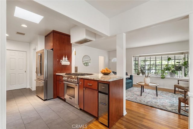 kitchen featuring a skylight, baseboards, light stone counters, premium appliances, and custom range hood