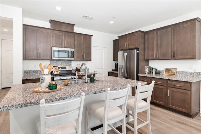 kitchen with a kitchen bar, appliances with stainless steel finishes, dark brown cabinets, a sink, and light wood finished floors