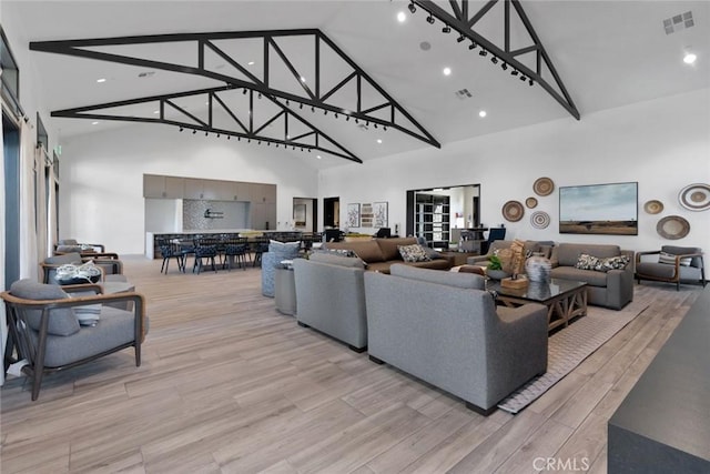 living area with visible vents, light wood finished floors, and high vaulted ceiling