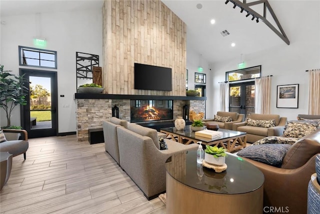 living room featuring high vaulted ceiling, a fireplace, light wood finished floors, and visible vents