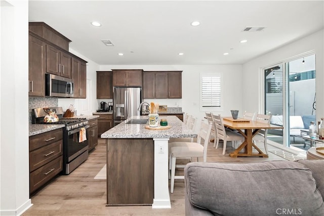 kitchen with a breakfast bar area, visible vents, appliances with stainless steel finishes, dark brown cabinets, and light wood-style flooring