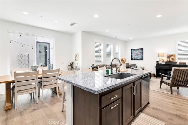 kitchen with visible vents, stainless steel dishwasher, dark brown cabinetry, a sink, and light wood finished floors