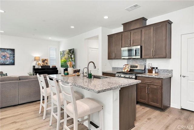 kitchen featuring dark brown cabinetry, a sink, light wood finished floors, stainless steel appliances, and open floor plan
