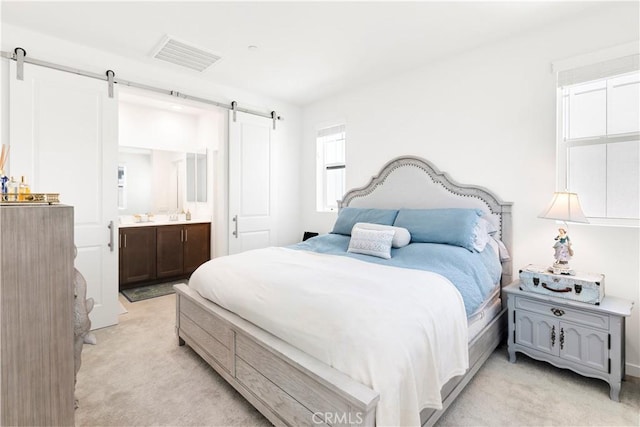 bedroom with visible vents, a barn door, ensuite bathroom, and light carpet