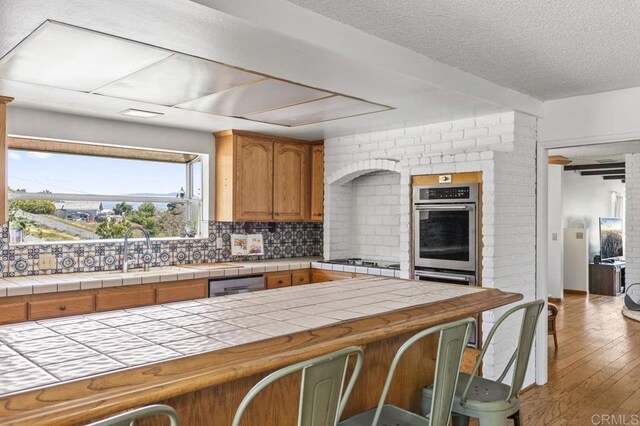 68256827 Kellyn Ln, Vista, CA 92084 - kitchen featuring brown cabinetry, tile counters, a textured ceiling, tasteful backsplash, and a sink