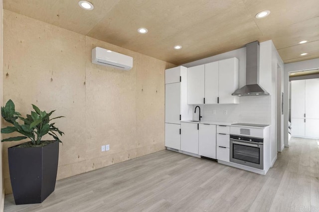68256827 Kellyn Ln, Vista, CA 92084 - kitchen featuring stainless steel oven, wall chimney range hood, a wall mounted AC, a sink, and light wood finished floors