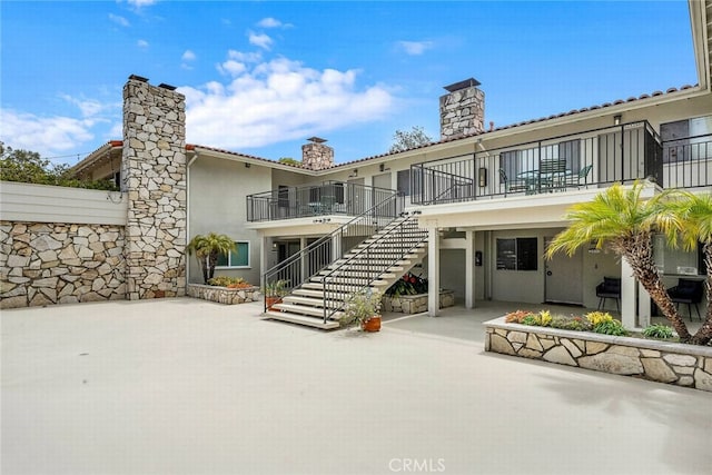 rear view of property with a patio area, stucco siding, a balcony, and a chimney