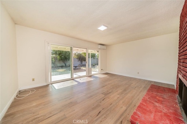 unfurnished living room featuring an AC wall unit, baseboards, a fireplace, and light wood-type flooring