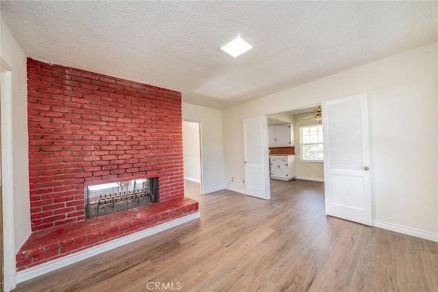 unfurnished living room with a fireplace, a textured ceiling, light wood-style flooring, a ceiling fan, and baseboards
