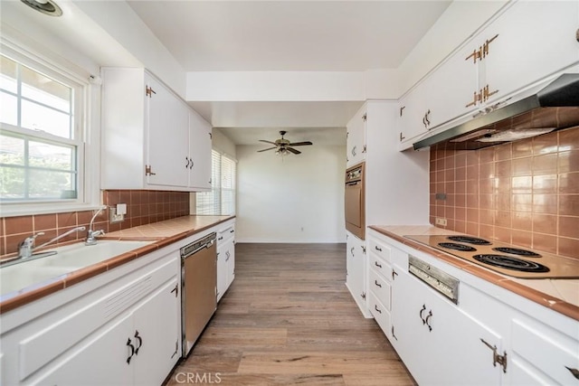 kitchen with a sink, electric stovetop, tile countertops, wall oven, and stainless steel dishwasher