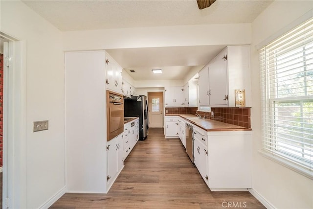 kitchen featuring white cabinets, appliances with stainless steel finishes, a sink, light wood finished floors, and decorative backsplash