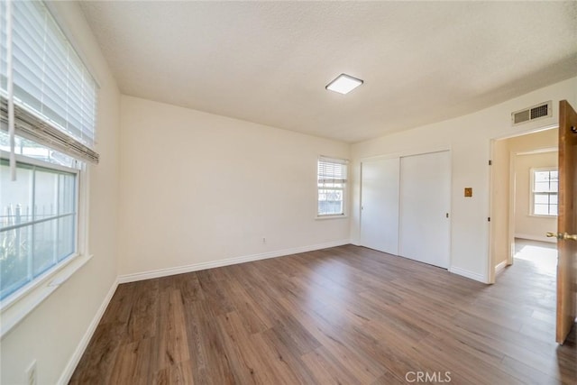 empty room with a healthy amount of sunlight, baseboards, wood finished floors, and visible vents