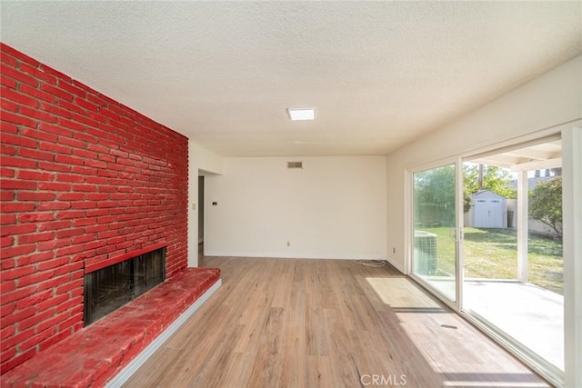 unfurnished living room with baseboards, a fireplace, a textured ceiling, and light wood-style flooring