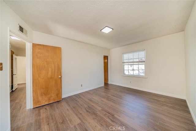 spare room with visible vents, a textured ceiling, baseboards, and wood finished floors