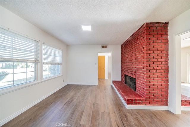 unfurnished living room with visible vents, a brick fireplace, light wood-style floors, baseboards, and a textured ceiling