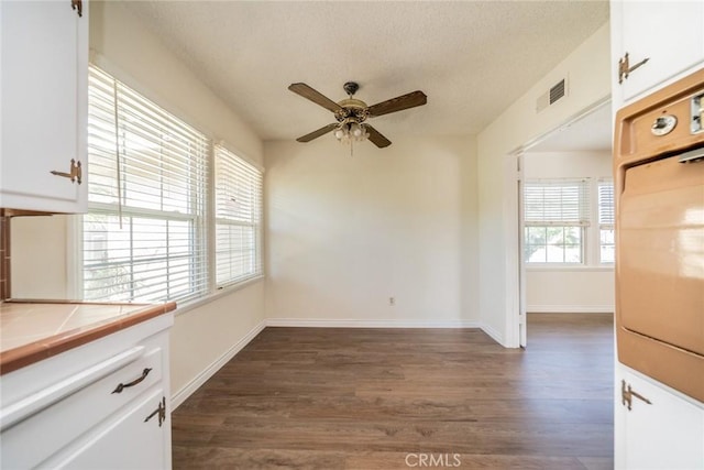 unfurnished dining area with visible vents, dark wood-style flooring, baseboards, a textured ceiling, and a ceiling fan