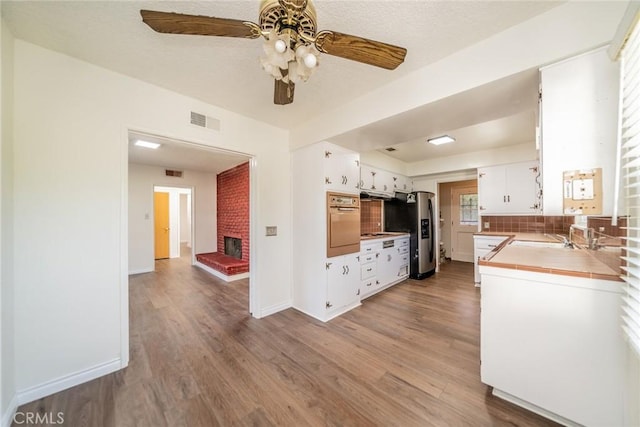 kitchen with visible vents, wall oven, stainless steel fridge, tile countertops, and a ceiling fan