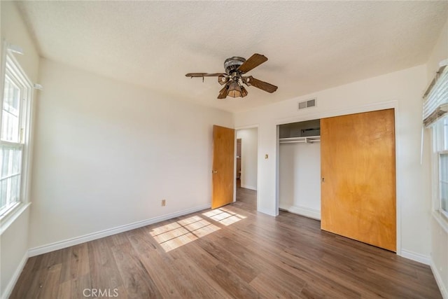 unfurnished bedroom with baseboards, visible vents, wood finished floors, and a closet