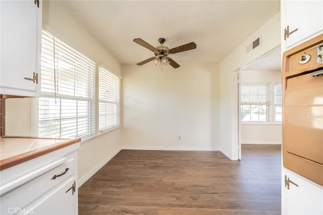 unfurnished dining area with baseboards, a ceiling fan, wood finished floors, and visible vents