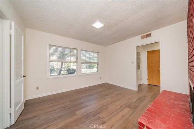 interior space with a textured ceiling, baseboards, wood finished floors, and visible vents