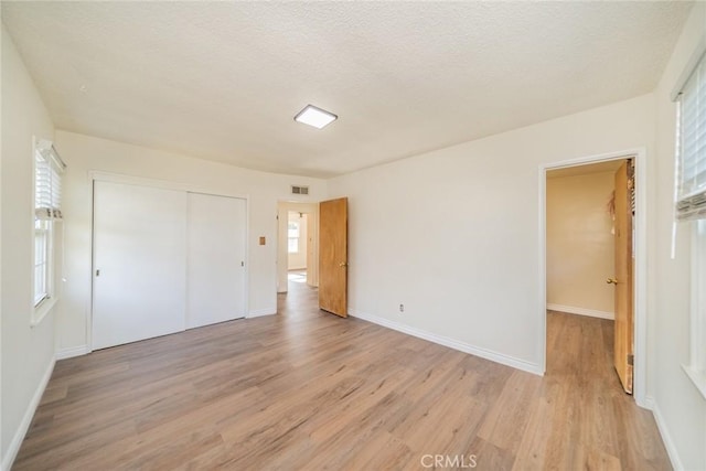 unfurnished bedroom featuring a textured ceiling, visible vents, baseboards, a closet, and light wood-style flooring