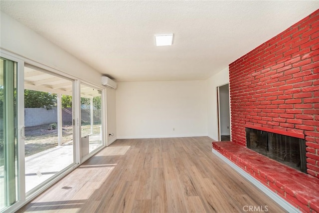 unfurnished living room with a brick fireplace, wood finished floors, baseboards, an AC wall unit, and a textured ceiling
