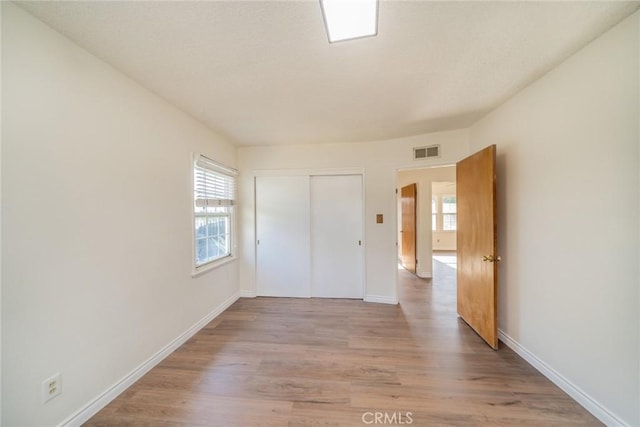 unfurnished bedroom with baseboards, visible vents, multiple windows, and light wood-style floors