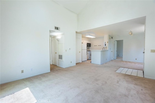 unfurnished living room with a high ceiling, visible vents, and light carpet