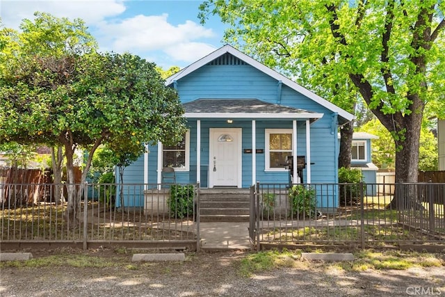 bungalow-style home featuring covered porch, a shingled roof, and a fenced front yard